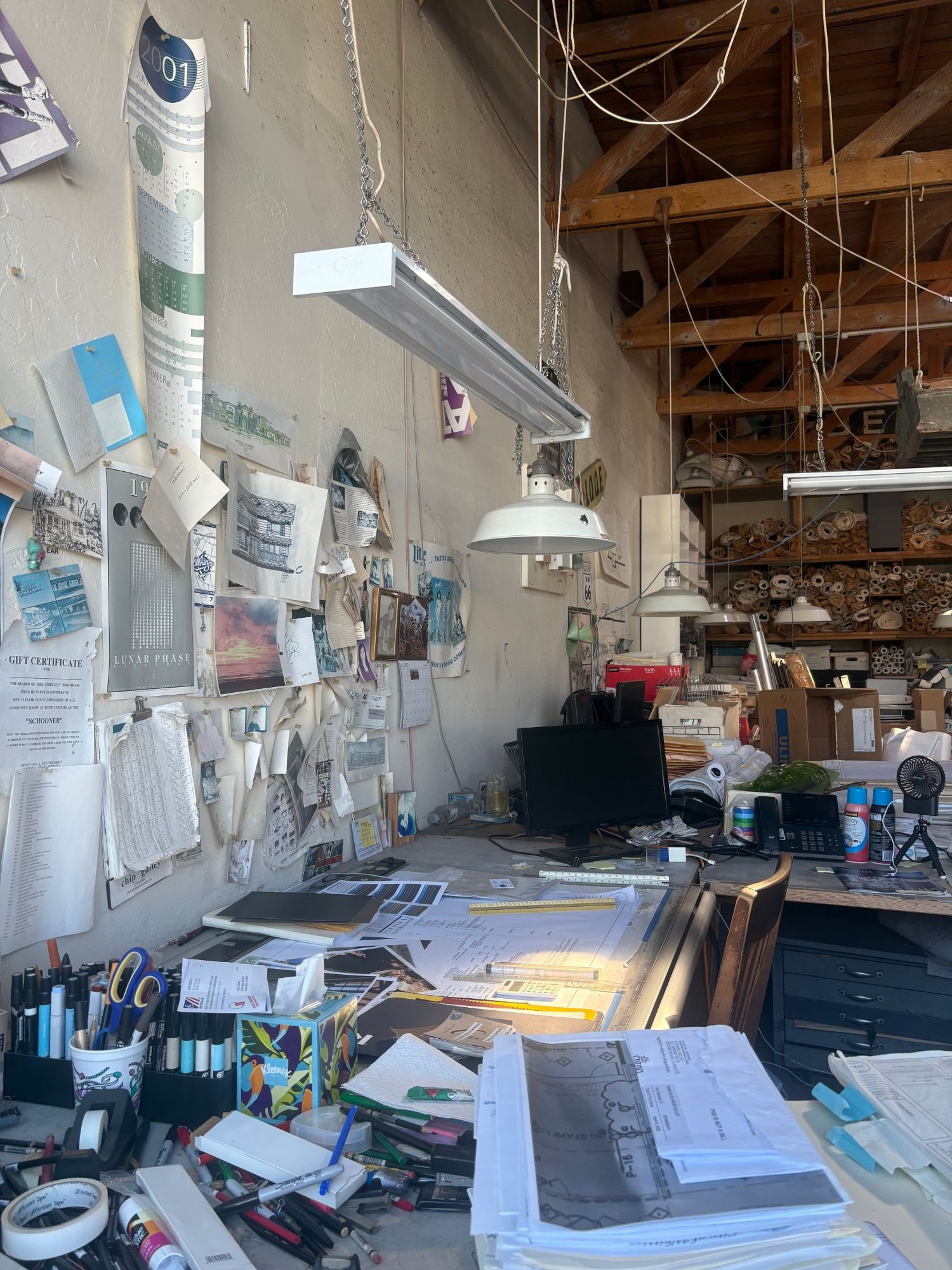 A working design studio: a pinned-up wall, hanging lamps and a desk covered in drawings